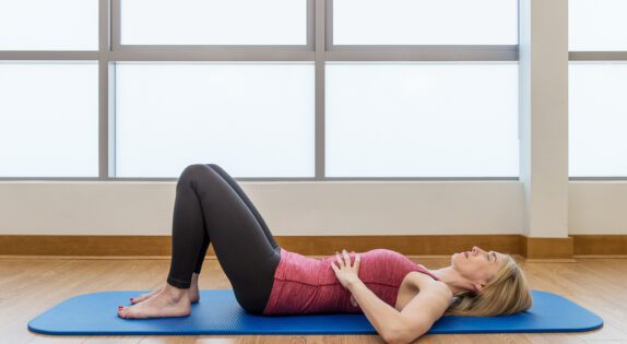 jeannie di bon is laid on a yoga mat with her knees bent
