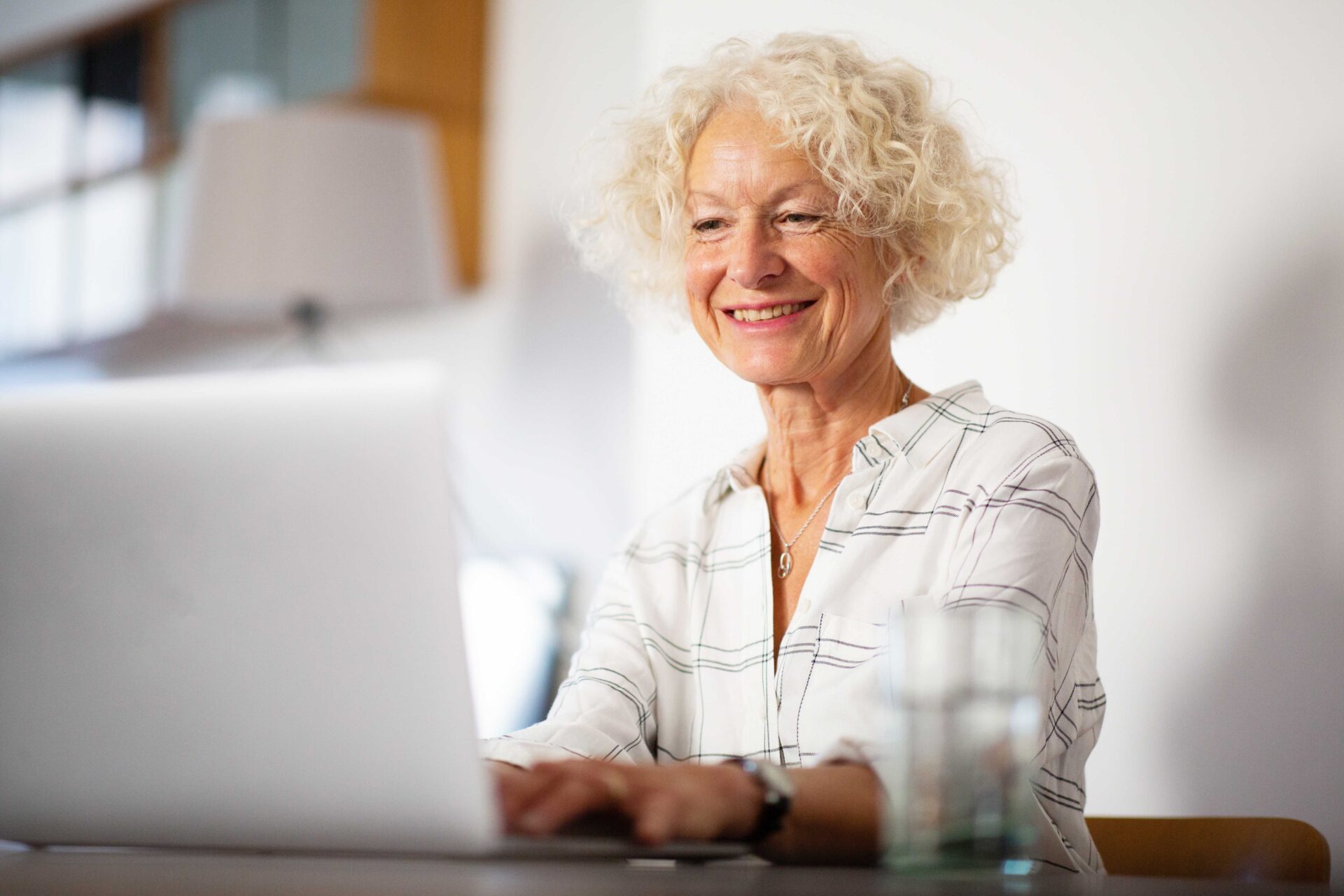 smiling-older-woman-sitting-at-home-using-laptop-c-2023-11-27-05-15-35-utc