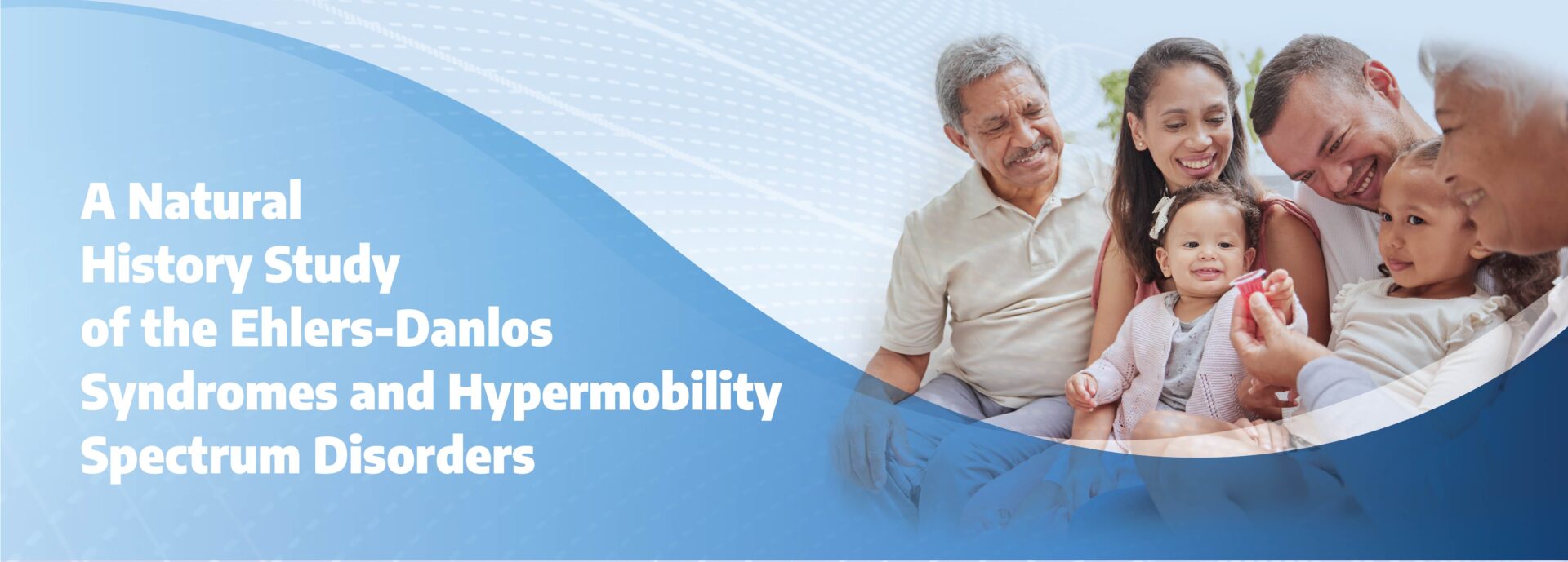 The image is a promotional banner featuring a family group and information on a medical study. On the left side, bold white text reads, "A Natural History Study of the Ehlers-Danlos Syndromes and Hypermobility Spectrum Disorders," set against a soft blue gradient background with a subtle dotted wave pattern. The right side of the image shows a family of diverse ages and ethnicities, gathered together with smiles. They appear to be enjoying a moment, with an older person offering a small red item to a young child seated at the center. The family members include two older adults, two parents, and two children, all warmly engaged with one another. The blue gradient background smoothly transitions towards the family photo, curving around the family on the right. This composition emphasizes a welcoming and inclusive atmosphere while promoting the study.